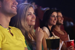Young woman sitting in cinema, watching movie, smiling.